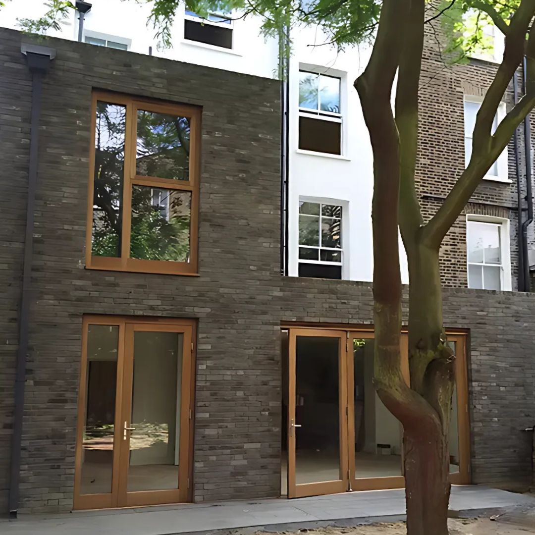 Modern brick building with wooden-framed windows and doors, surrounded by greenery